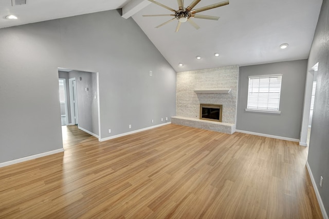 unfurnished living room featuring beamed ceiling, a large fireplace, ceiling fan, and light wood-type flooring