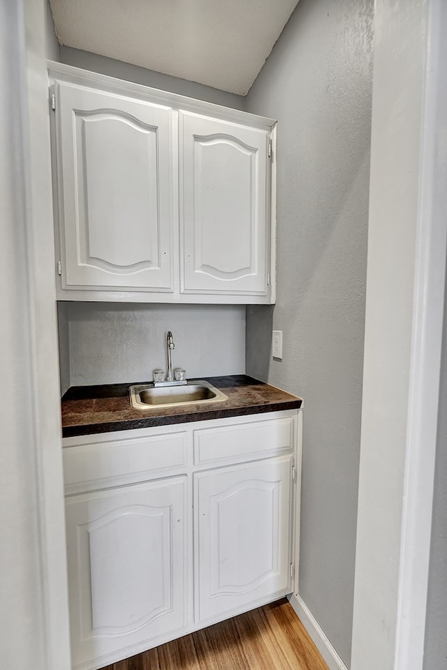 bar with white cabinetry, sink, and light hardwood / wood-style floors