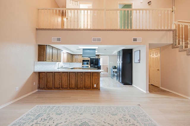 kitchen featuring kitchen peninsula, a towering ceiling, light hardwood / wood-style flooring, backsplash, and black fridge