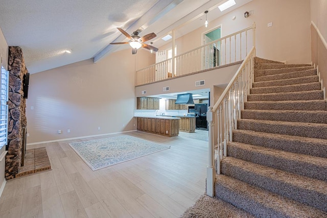 unfurnished living room featuring light hardwood / wood-style floors, high vaulted ceiling, ceiling fan, and a textured ceiling