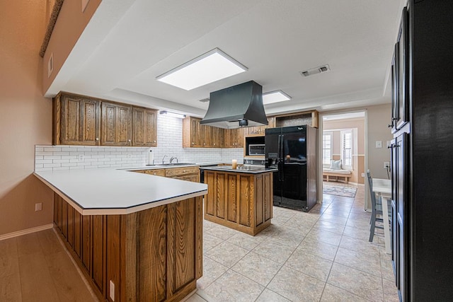 kitchen with sink, black refrigerator with ice dispenser, island range hood, kitchen peninsula, and decorative backsplash