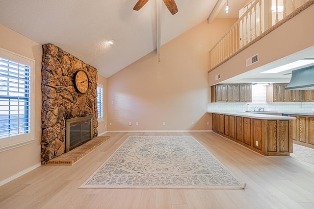 kitchen with light wood-type flooring, plenty of natural light, custom range hood, and a fireplace