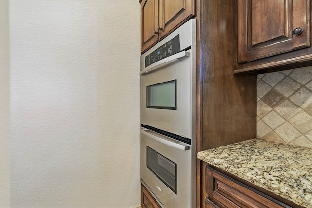 5001 Crista Ln, Midland, TX 79707 - kitchen featuring stainless steel double oven, light stone counters, decorative backsplash, and dark brown cabinets