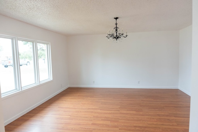 spare room with a textured ceiling, an inviting chandelier, and light hardwood / wood-style flooring