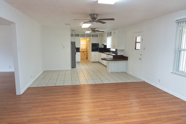 kitchen with white cabinetry, stainless steel fridge, oven, light hardwood / wood-style floors, and a textured ceiling