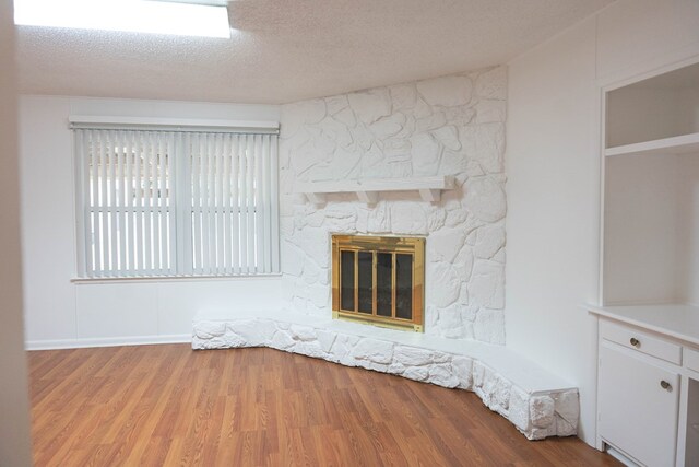 unfurnished living room with a stone fireplace, a textured ceiling, and light hardwood / wood-style flooring