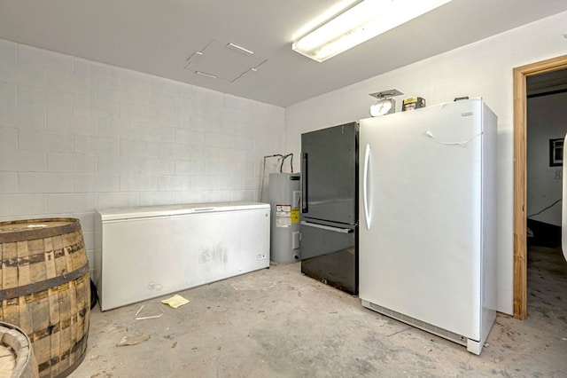 kitchen featuring concrete floors, light countertops, freestanding refrigerator, electric water heater, and concrete block wall