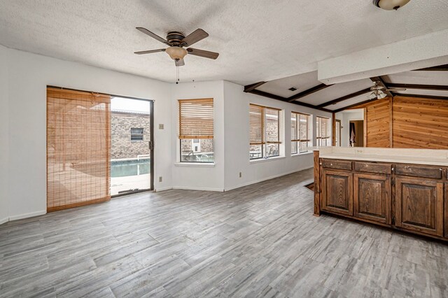 interior space with a textured ceiling, ceiling fan, light wood-style floors, baseboards, and vaulted ceiling with beams