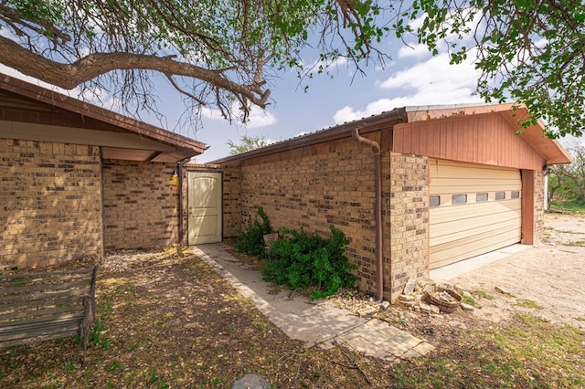 view of property exterior with a garage, brick siding, fence, and dirt driveway