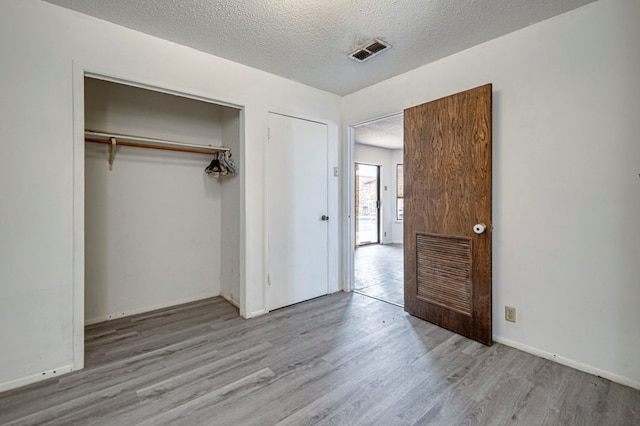 unfurnished bedroom featuring wood finished floors, a closet, baseboards, visible vents, and a textured ceiling