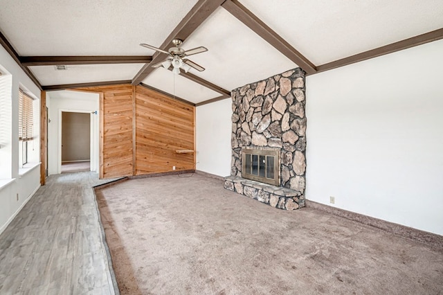 unfurnished living room featuring ceiling fan, vaulted ceiling with beams, a stone fireplace, wood walls, and wood finished floors