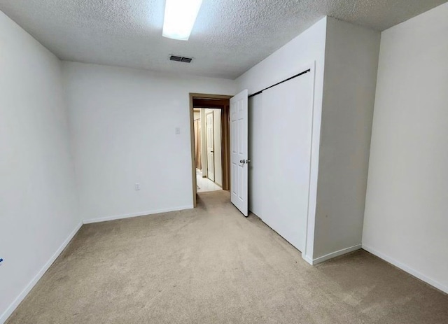 unfurnished bedroom with light carpet, baseboards, visible vents, a textured ceiling, and a closet