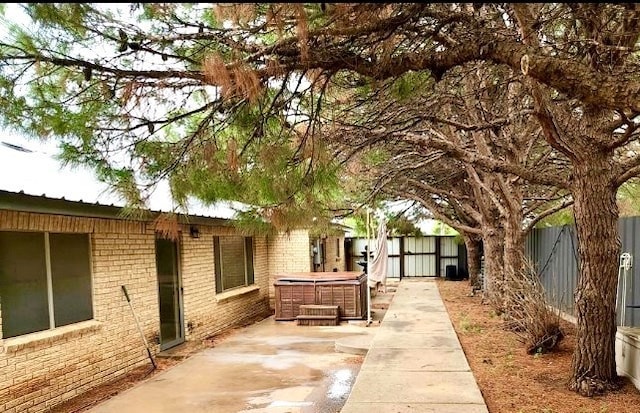 exterior space featuring brick siding, a patio area, fence private yard, and a hot tub