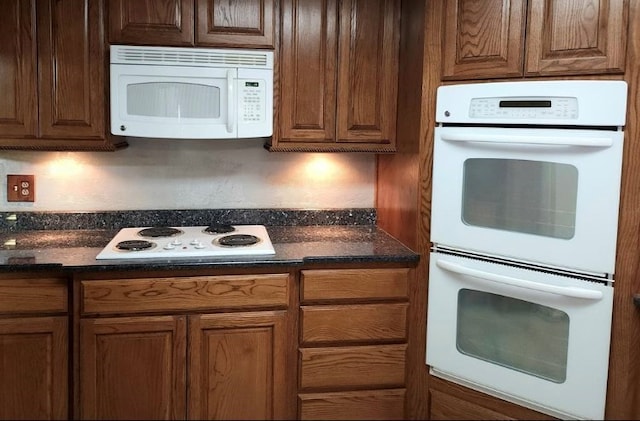 kitchen featuring white appliances, dark stone countertops, and brown cabinets