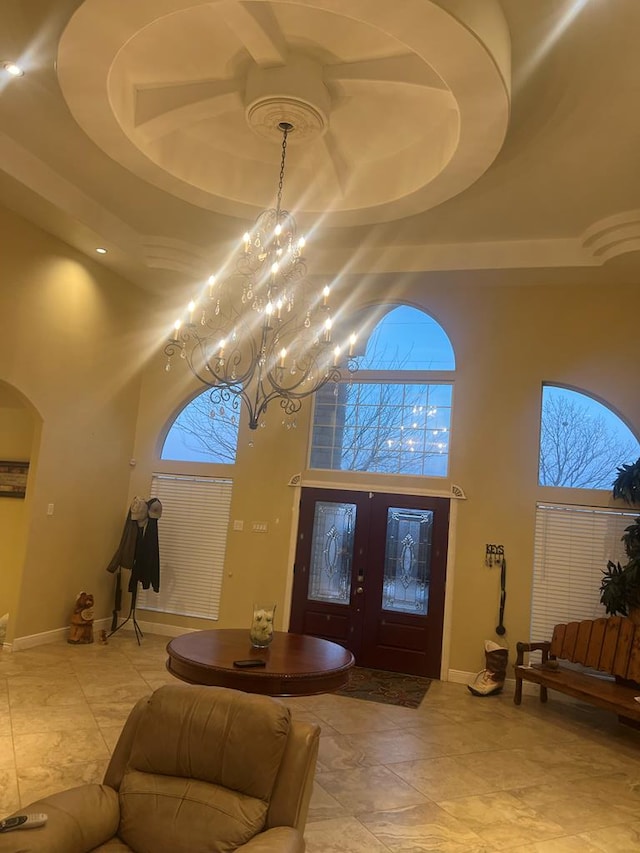 foyer entrance featuring arched walkways, baseboards, a raised ceiling, and a towering ceiling