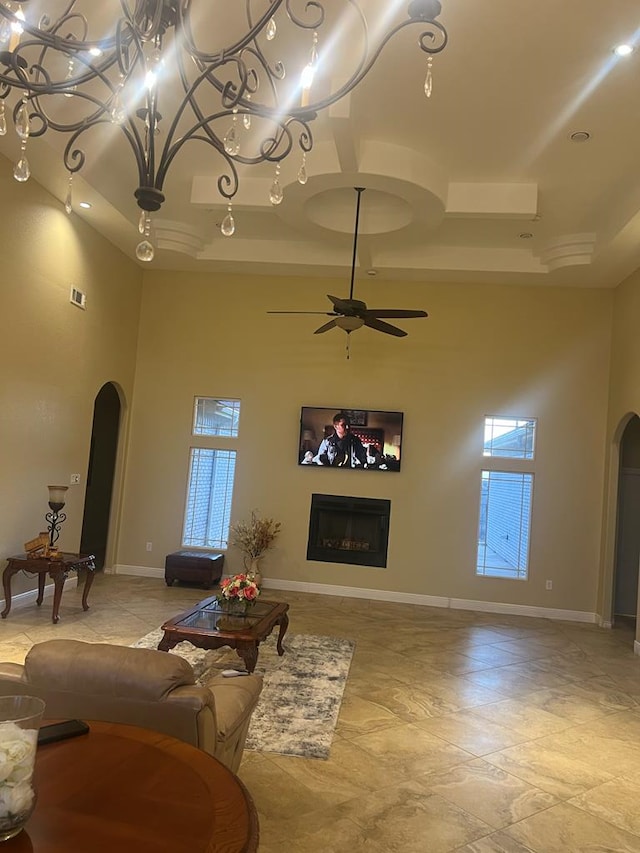 living area featuring baseboards, arched walkways, a raised ceiling, and a glass covered fireplace