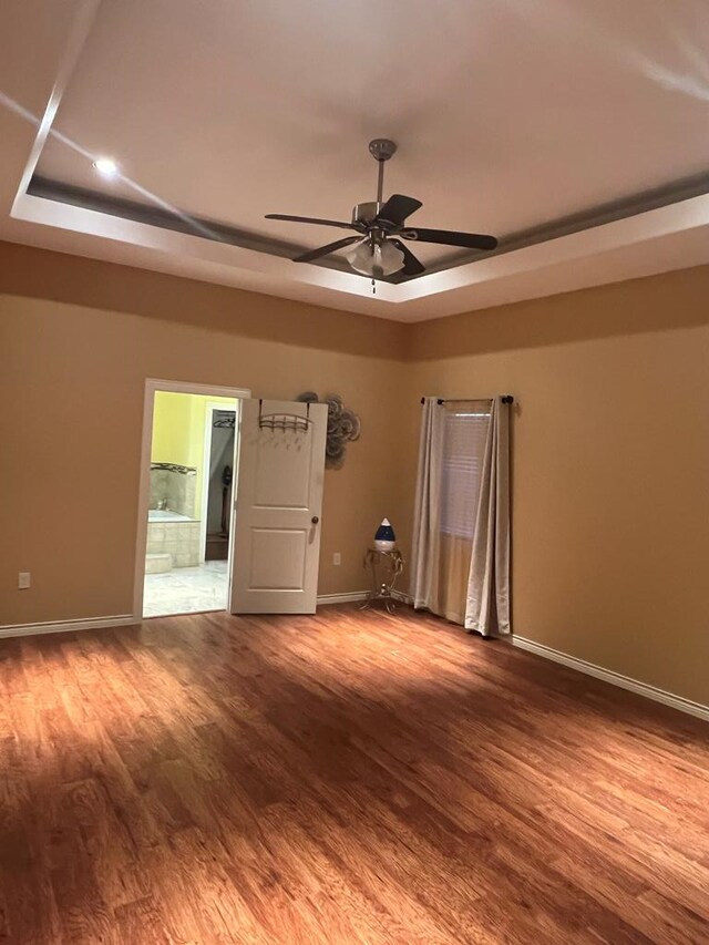 empty room featuring baseboards, a tray ceiling, and wood finished floors