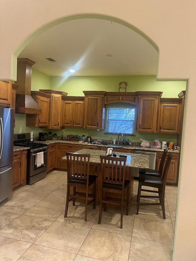 kitchen featuring visible vents, stone countertops, appliances with stainless steel finishes, a kitchen bar, and wall chimney exhaust hood