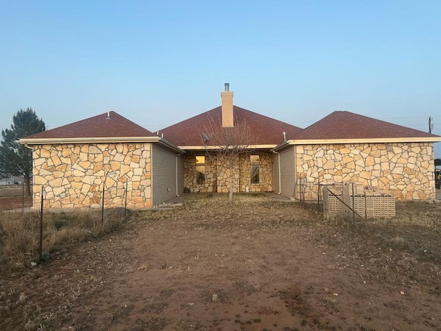 rear view of house featuring stone siding and a chimney