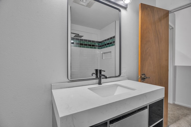 full bath with tiled shower, vanity, and a textured wall