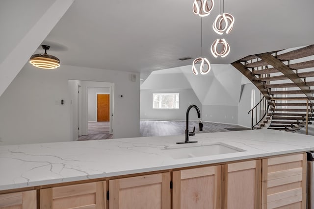 kitchen featuring visible vents, a sink, open floor plan, light brown cabinetry, and light stone counters