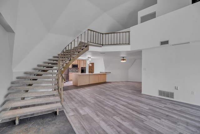 staircase featuring wood finished floors, a towering ceiling, and visible vents