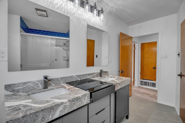 full bath featuring a shower with shower door, double vanity, visible vents, and a sink