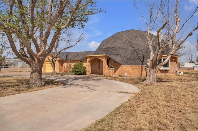 view of front of home with roof with shingles, brick siding, and curved driveway