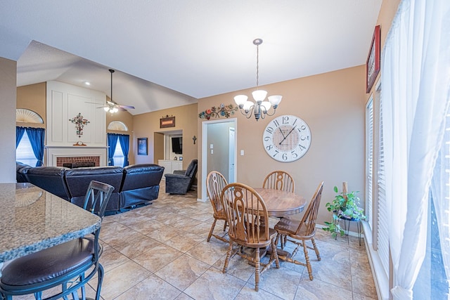 dining room featuring lofted ceiling, a chandelier, a brick fireplace, healthy amount of natural light, and ceiling fan