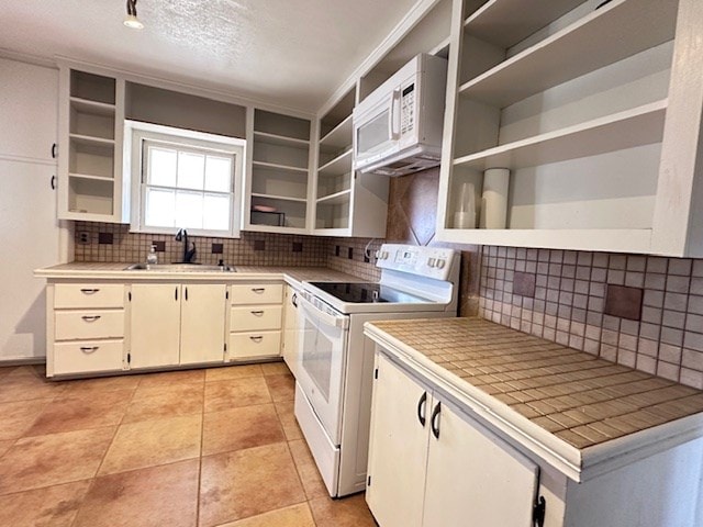 kitchen with white appliances, tile counters, open shelves, and a sink