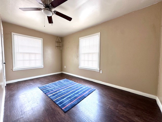 spare room featuring a ceiling fan, dark wood-style flooring, and baseboards