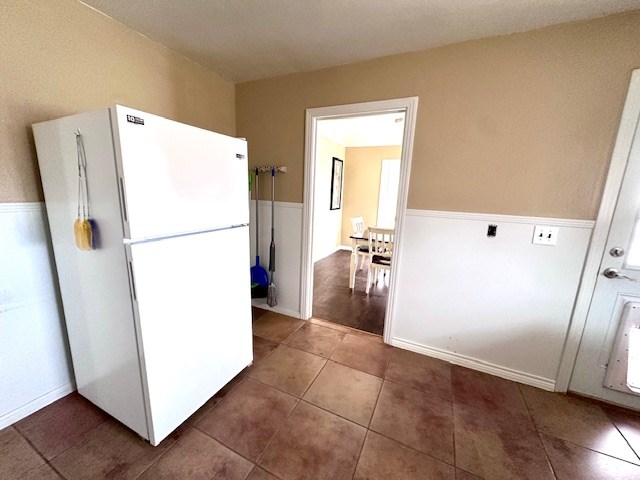 kitchen featuring freestanding refrigerator, a wainscoted wall, and dark tile patterned floors