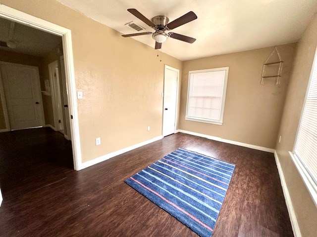 empty room featuring dark wood-style floors, visible vents, baseboards, and a ceiling fan