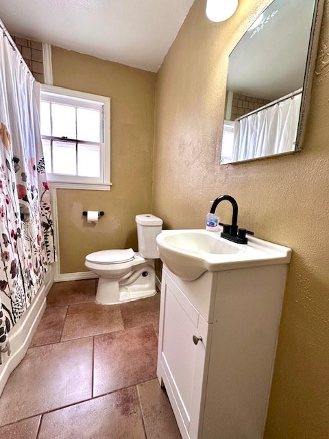 full bath featuring stone tile flooring, a textured wall, vanity, and toilet