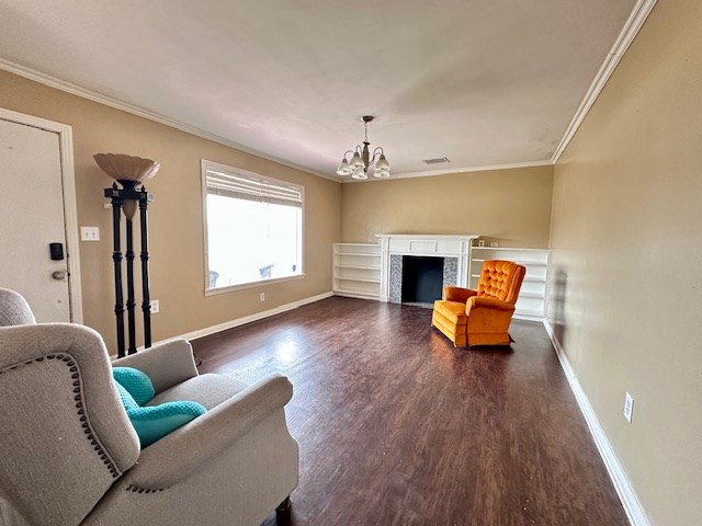 living room with baseboards, dark wood-style floors, crown molding, a fireplace, and a chandelier