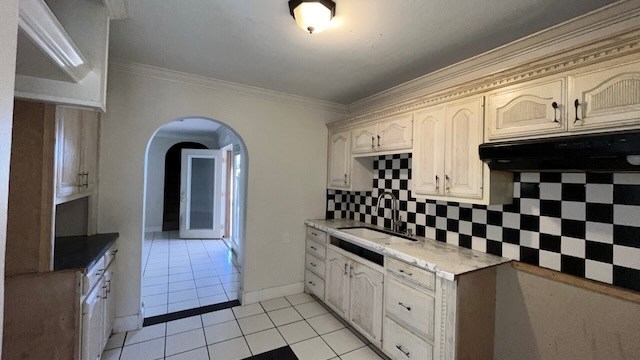 kitchen featuring light tile patterned flooring, tasteful backsplash, ornamental molding, and sink