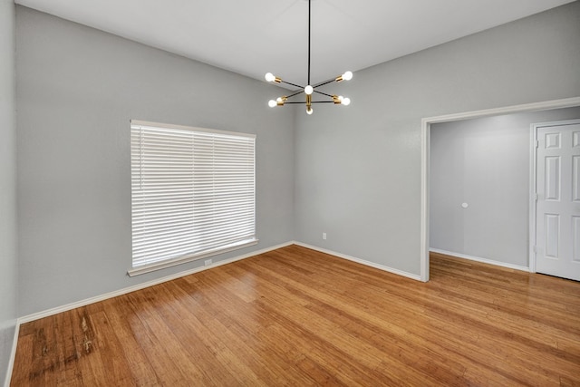 spare room featuring baseboards, an inviting chandelier, and wood finished floors