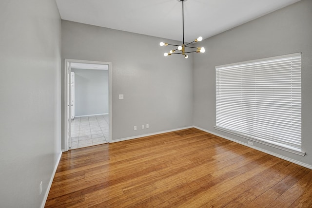 spare room with an inviting chandelier, baseboards, and light wood finished floors