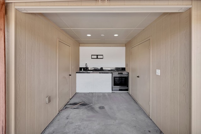 kitchen featuring a sink, stainless steel range with gas stovetop, unfinished concrete floors, and wood walls