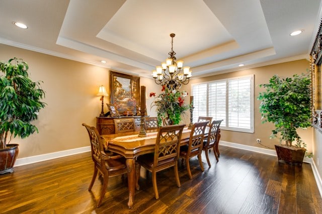 dining area featuring a raised ceiling, a chandelier, dark hardwood / wood-style floors, and ornamental molding