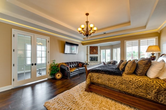 bedroom with access to exterior, an inviting chandelier, dark hardwood / wood-style floors, a tray ceiling, and a fireplace