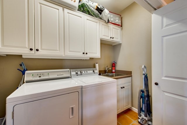 laundry area with cabinets, independent washer and dryer, light tile patterned floors, and sink