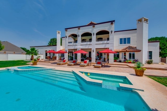 back of house with a swimming pool with hot tub, a balcony, and a patio