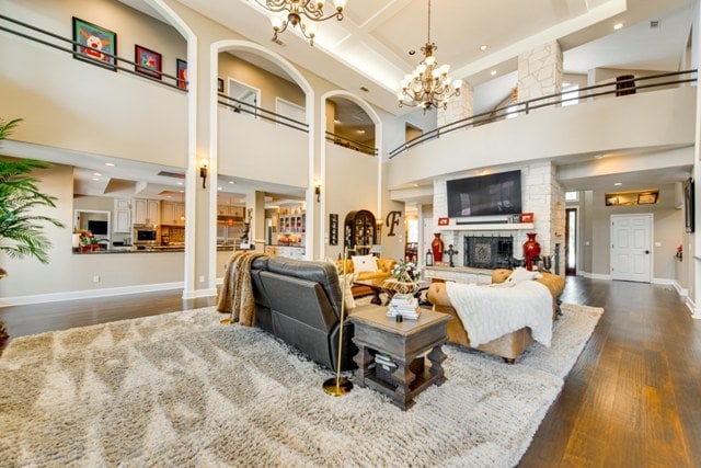 living room featuring a stone fireplace, dark hardwood / wood-style flooring, a towering ceiling, and beamed ceiling