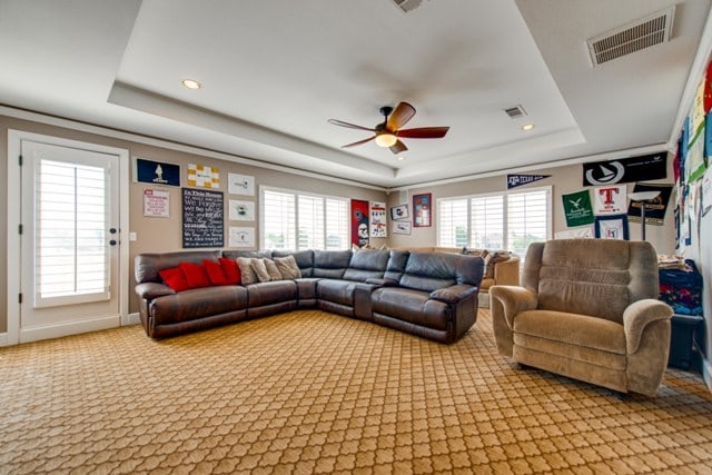 carpeted living room with ceiling fan, a healthy amount of sunlight, and a tray ceiling