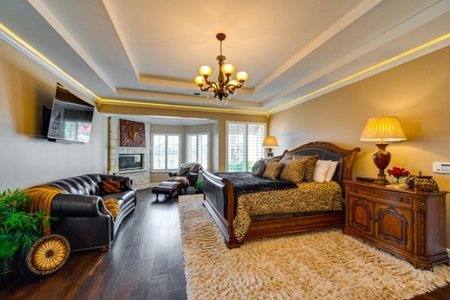 bedroom with a tray ceiling, a fireplace, hardwood / wood-style floors, and an inviting chandelier