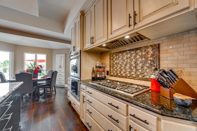 kitchen with backsplash, stainless steel appliances, dark stone counters, and dark wood-type flooring