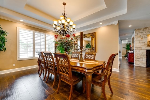 dining room featuring an inviting chandelier, dark hardwood / wood-style flooring, a stone fireplace, and a tray ceiling