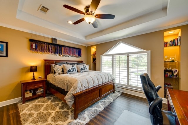 bedroom with ornamental molding, a raised ceiling, ceiling fan, and dark wood-type flooring