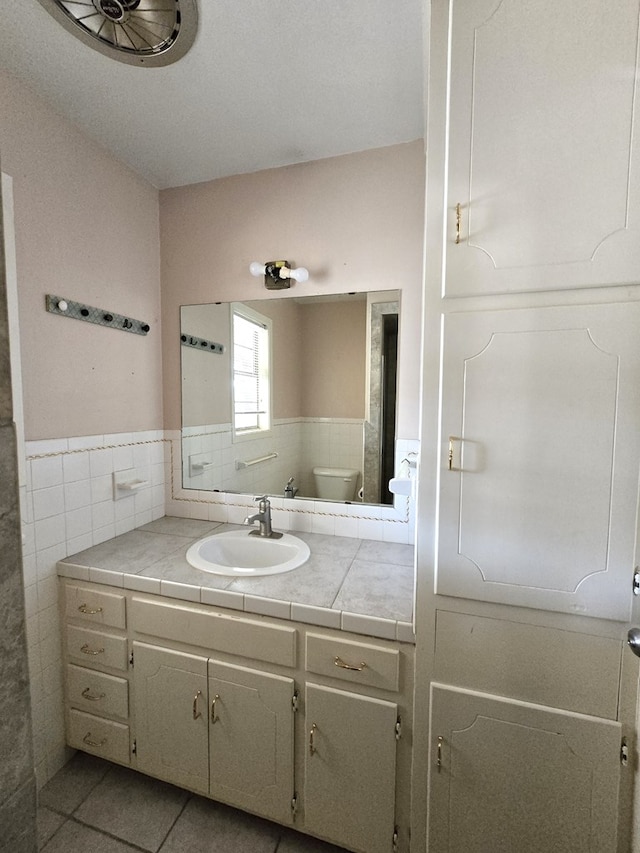 bathroom featuring tile patterned flooring, vanity, tile walls, and toilet